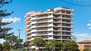 Un immeuble à plusieurs étages, doté de balcons, entouré d’arbres et surplombant un ciel dégagé.