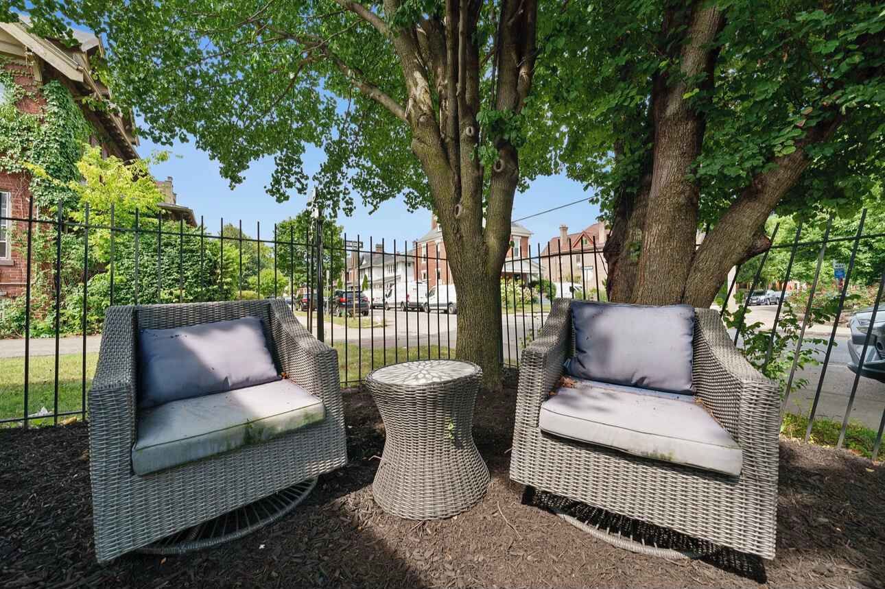 Two wicker sofas with cushions, a round wicker table, and a large tree providing shade.