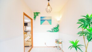 Ein heller Korridor mit Holzboden, weißer Wand, Holztür, einer Pendelleuchte, einem gerahmten Bild und einem Blumentopf.