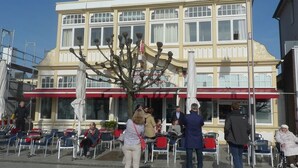 A multi-story building with a balcony and a large tree in front.