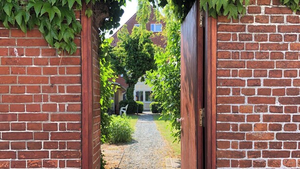 A brick pathway leading to a wooden gate with a metal mesh.