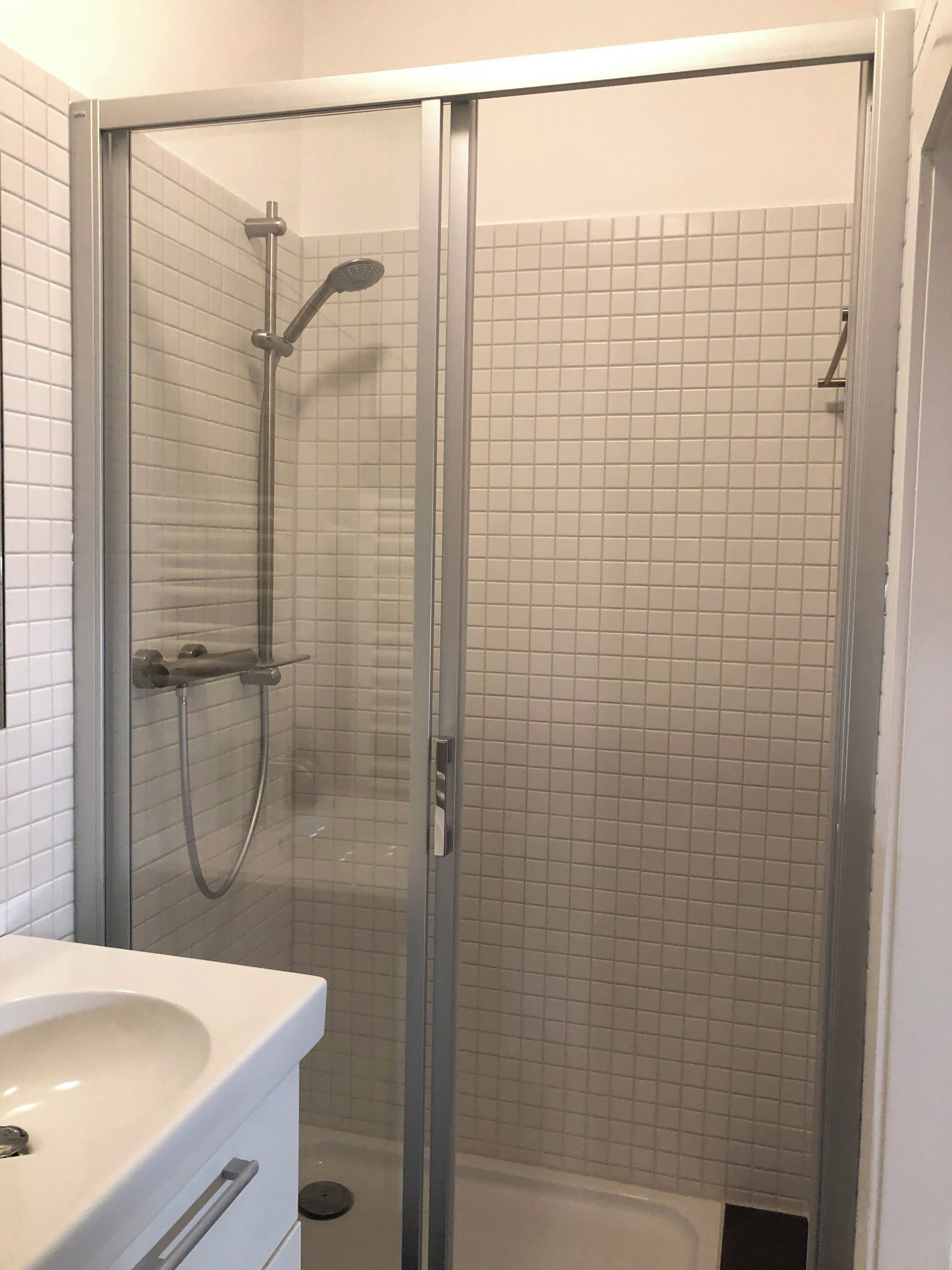 A glass-enclosed shower with a handheld showerhead and a wall-mounted faucet.