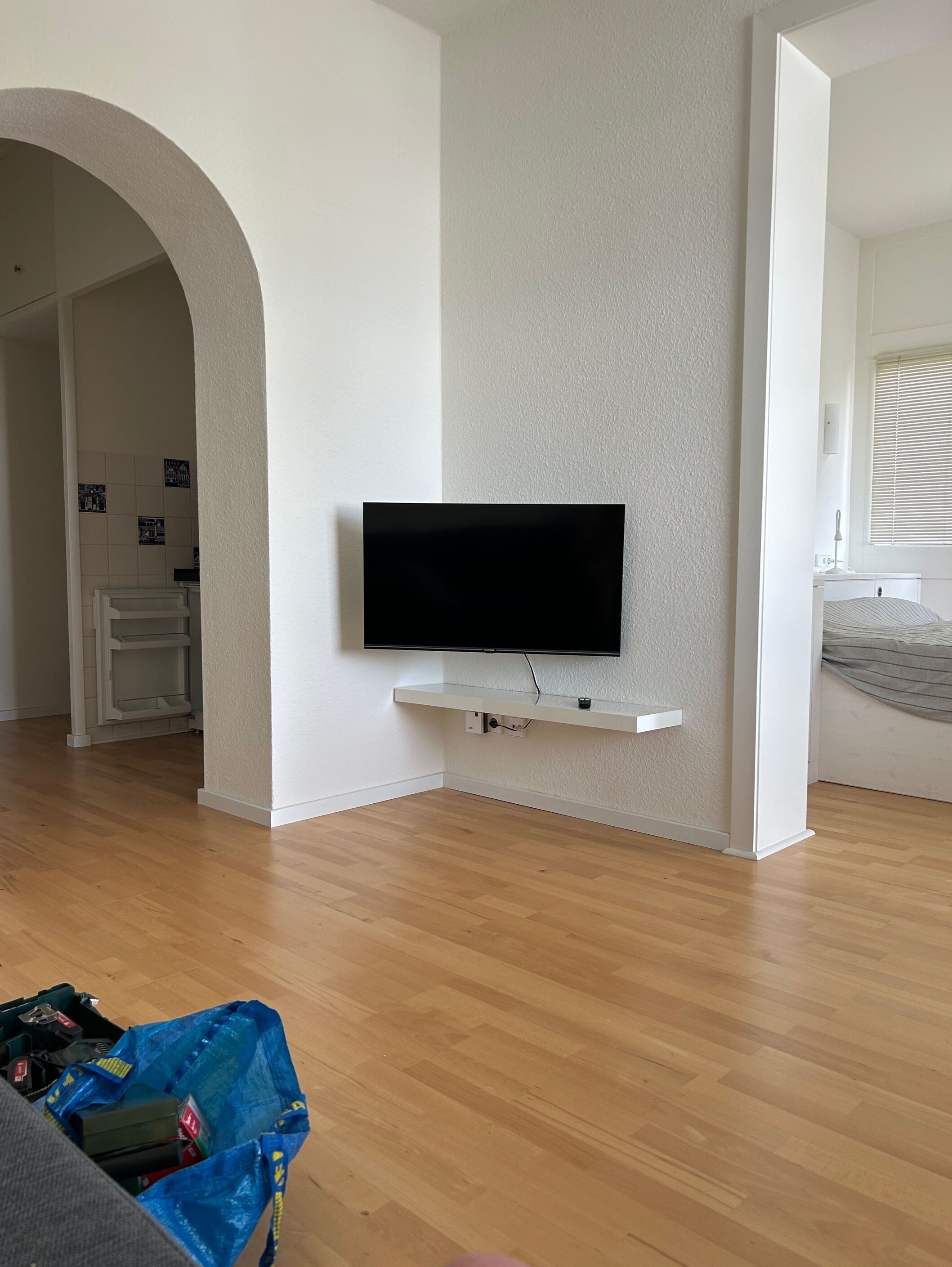 A modern living room with a flat-screen TV mounted on a white wall, wooden flooring, and a blue storage bin on the floor.