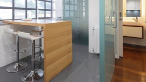 Une cuisine moderne avec un plan de travail en bois, des tabourets de bar en acier inoxydable et une cloison en verre.