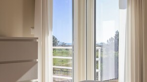 Une chambre avec une grande fenêtre, un lit et une vue sur un balcon doté d’une balustrade.
