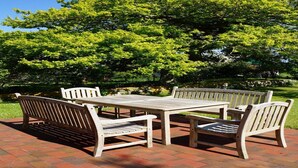 Un patio con tavolo e quattro panche, circondato da rigogliosi alberi verdi.