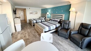 Et lille hotelværelse med en seng, to stole, et lille bord og et skrivebord.