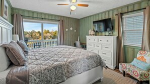 A bedroom with a bed, dresser, TV, and a balcony with a view. - Channeling The Sun-4BR/2BA Channel House- Pets (North Myrtle Beach)