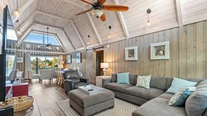 A spacious living area with a high ceiling, wooden walls, and a large sofa. - Channeling The Sun-4BR/2BA Channel House- Pets (North Myrtle Beach)