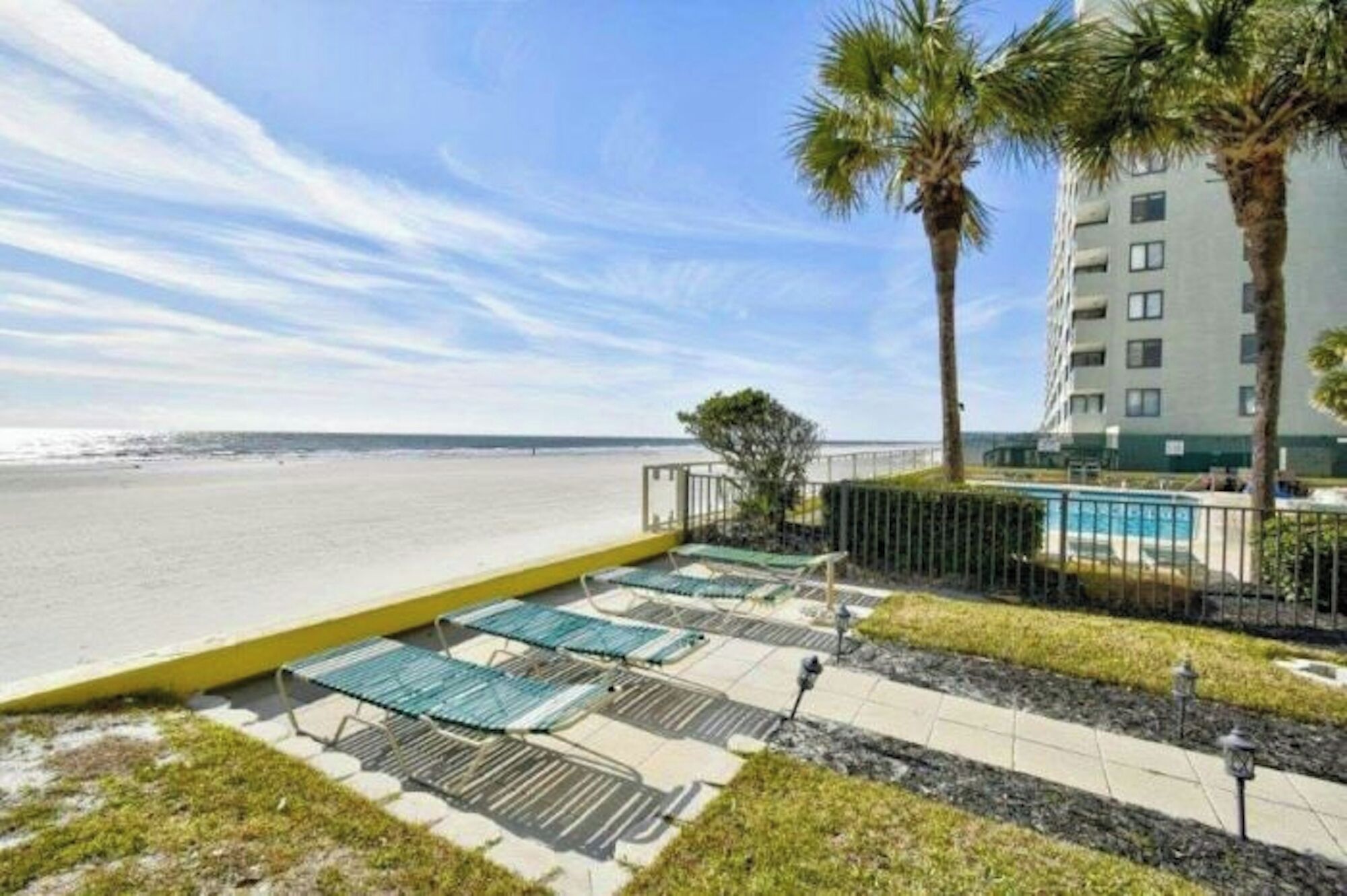 A beachfront property with a pool area, palm trees, and a view of the ocean.