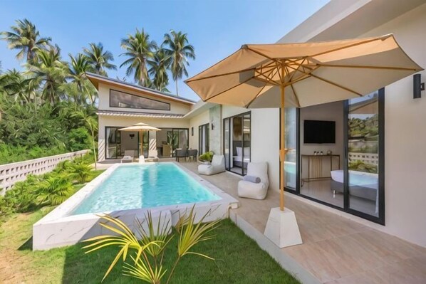 Una casa moderna con piscina, mobiliario exterior y una gran pantalla de televisión.