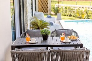 Una mesa con una planta en maceta, dos tazas de café y un plato de pasteles junto a una piscina.