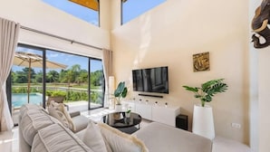 A modern living room with a large sofa, a flat-screen TV, and a view of a swimming pool. - Sereniwood 2 - 3BR Villa with Private Pool (Koh Samui)