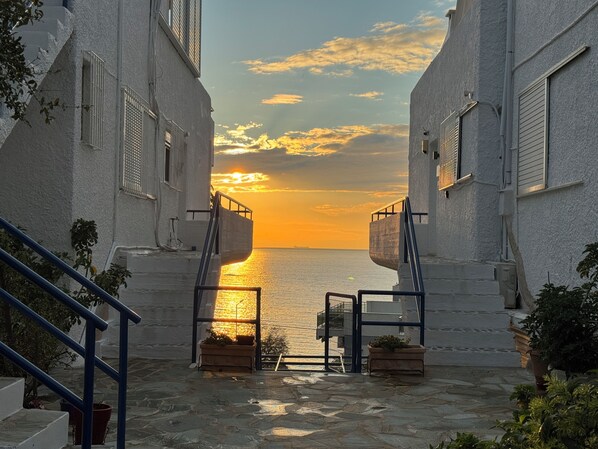 A narrow pathway leading to a body of water with a sunset in the background. - Panoramic Seaview Maisonette with Garden steps from the beach (Saronida)