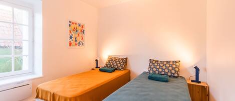 A room with two single beds, a window, a radiator, and a wall decoration.