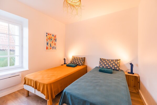 A room with two single beds, a window, a radiator, and a wall decoration.