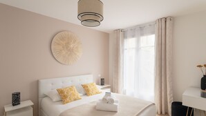 Ein modernes Hotelzimmer mit einem ordentlich bezogenen Bett, einem Nachttisch mit Lampe und einem großen Fenster mit Vorhängen.
