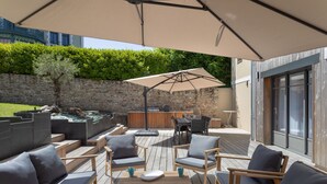 Eine Terrasse im Freien mit Holzmöbeln, einem großen Sonnenschirm und einer Steinmauer.
