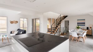Eine moderne Küche mit einer zentralen Kochinsel, einem Essbereich mit Tisch und Stühlen sowie einer Treppe, die zu einer oberen Ebene führt.