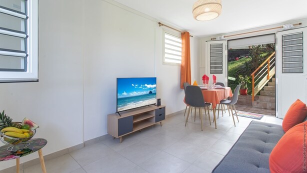 A modern living room with a flat-screen TV, a dining area with a table and chairs, and a staircase leading to an outdoor area.