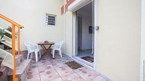 A small patio with a table and chairs, a sliding glass door, and a staircase with orange railings.