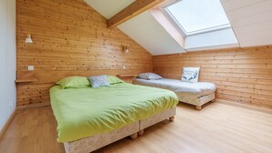 A room with a sloped ceiling, wooden walls, a skylight, two beds, and a small window.