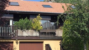 A two-story building with a brown garage door, a wooden fence, and a staircase leading to a balcony.