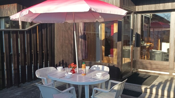 A patio with a table and chairs, a pink umbrella, and a glass door leading to an interior space.