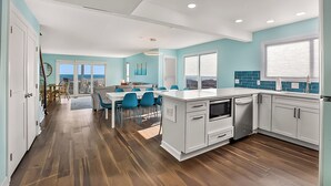 A modern kitchen with white cabinets, a large island, and a dining area with blue chairs. - Twin Palms Beach House (Sleeps up to 26) (North Myrtle Beach)