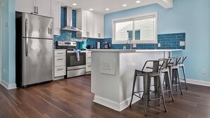 A modern kitchen with a stainless steel refrigerator, a built-in oven, and a blue-tiled backsplash. - Twin Palms Beach House (Sleeps up to 26) (North Myrtle Beach)