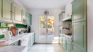 Una cocina con armarios verdes, encimera blanca y puerta que da a un patio.