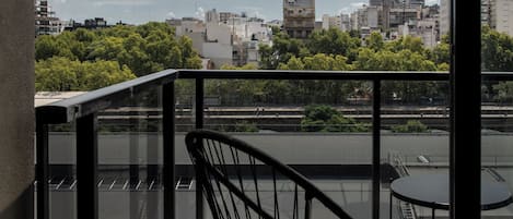 Un balcón con una silla y una mesa de metal, con vistas a un paisaje urbano con edificios y árboles.