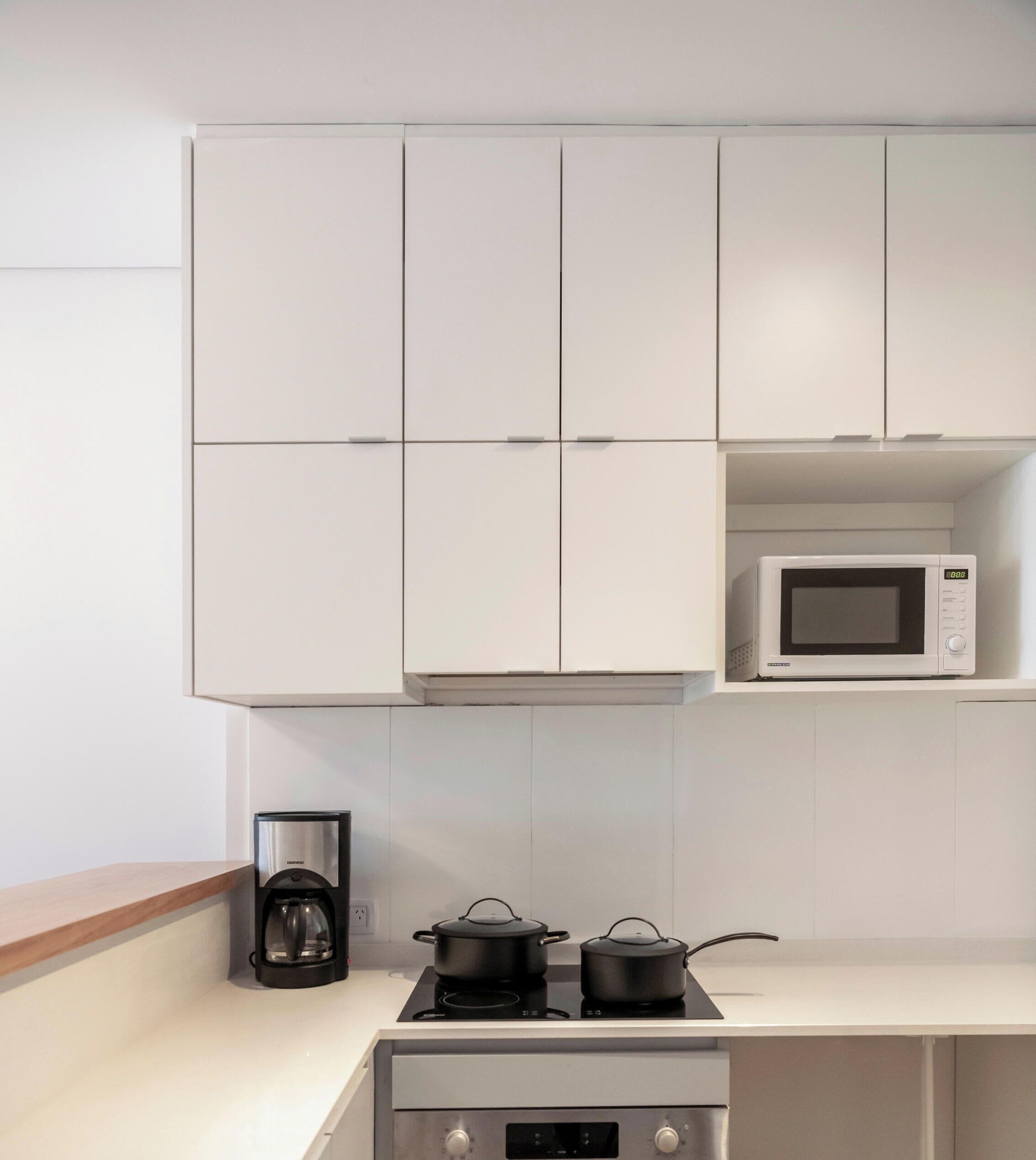 A kitchen with white cabinets, a microwave, a coffee maker, and a stove.