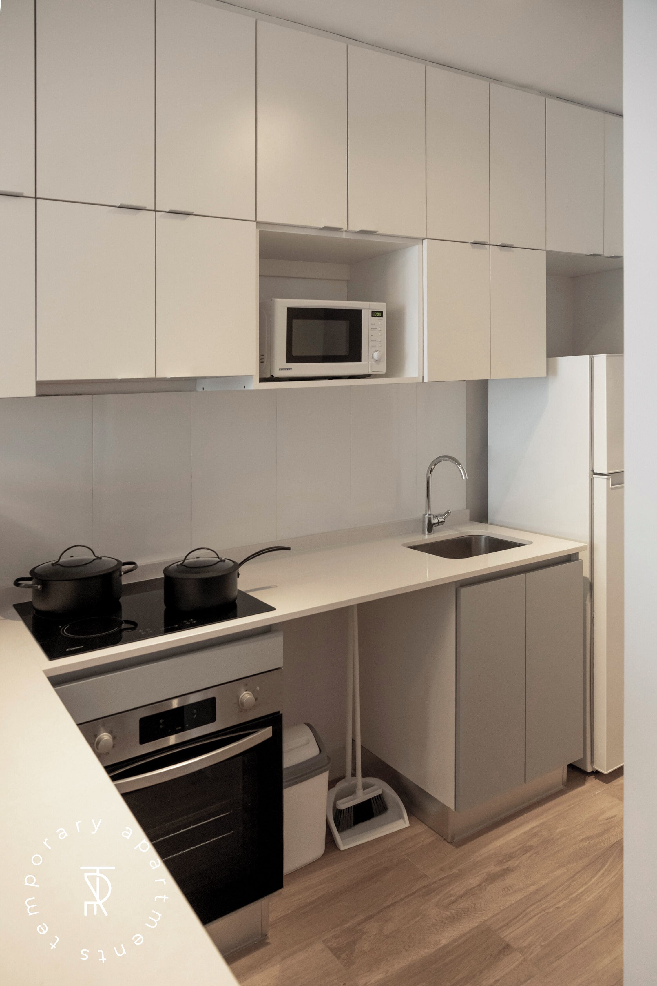 Eine moderne Küche mit weißen Schränken, einer Mikrowelle, einem Spülbecken, einem Herd und einem Backofen.