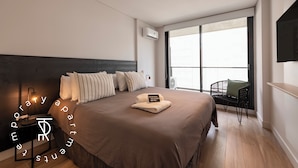A modern hotel room with a large bed, a bedside table, a chair, a TV, and a window with a view. - Top Rentals Palermo Soho (Buenos Aires)