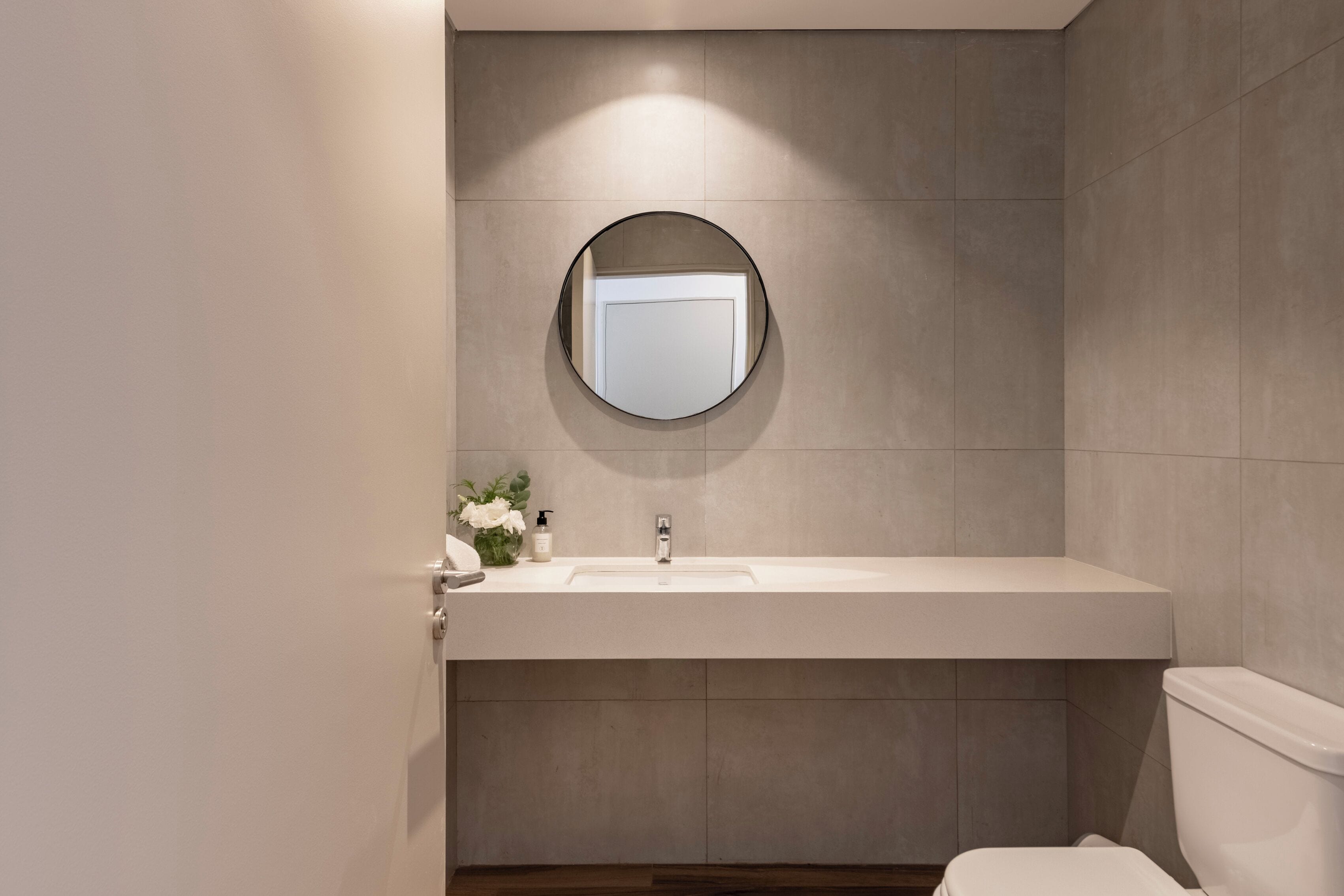Une salle de bain moderne avec un miroir rond, un lavabo blanc et des toilettes.