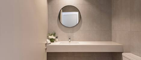 Une salle de bain moderne avec un miroir rond, un lavabo blanc et des toilettes.