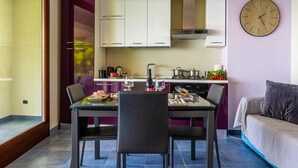 Une cuisine de taille réduite avec des meubles blancs, une table à manger avec des chaises, une horloge au mur et un canapé dans un coin.