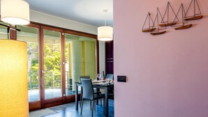 Un coin repas avec une table dressée pour deux personnes, une porte-fenêtre coulissante donnant sur un balcon et une décoration murale en forme de balance.