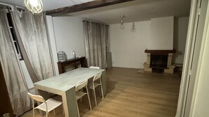 A spacious room with a wooden floor, a dining table with chairs, a fireplace, and a ceiling fan. - Appartio - Large house near PARIS (Villiers-le-Bel)
