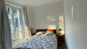 A bedroom with a bed, a nightstand, a lamp, and a window with curtains. - Appartio - Large house near PARIS (Villiers-le-Bel)