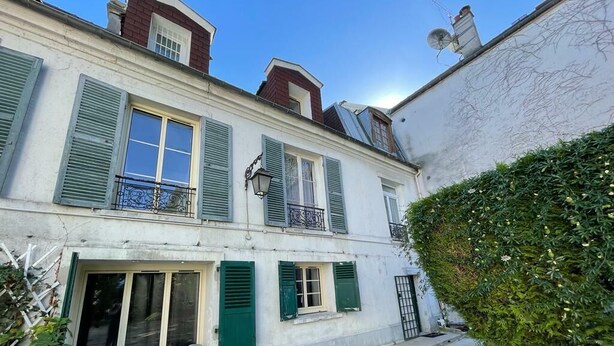 A two-story building with green shutters, a balcony with a wrought iron railing, and a small outdoor seating area with chairs. - Appartio - Large house near PARIS (Villiers-le-Bel)