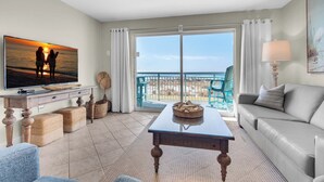 A living room with a TV, sofa, and a balcony with a view of the ocean.