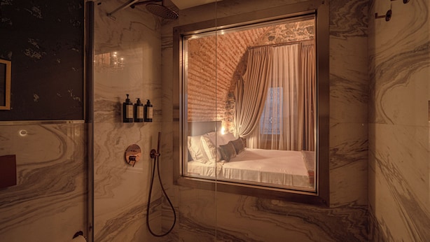 A bathroom with a glass shower enclosure, marble walls, a toilet paper holder, and a window with curtains. - Stone Inn Galata (Istanbul)
