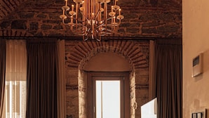 A room with a stone wall, wooden floor, a chandelier, a window with curtains, and a television on a stand. - Stone Inn Galata (Istanbul)
