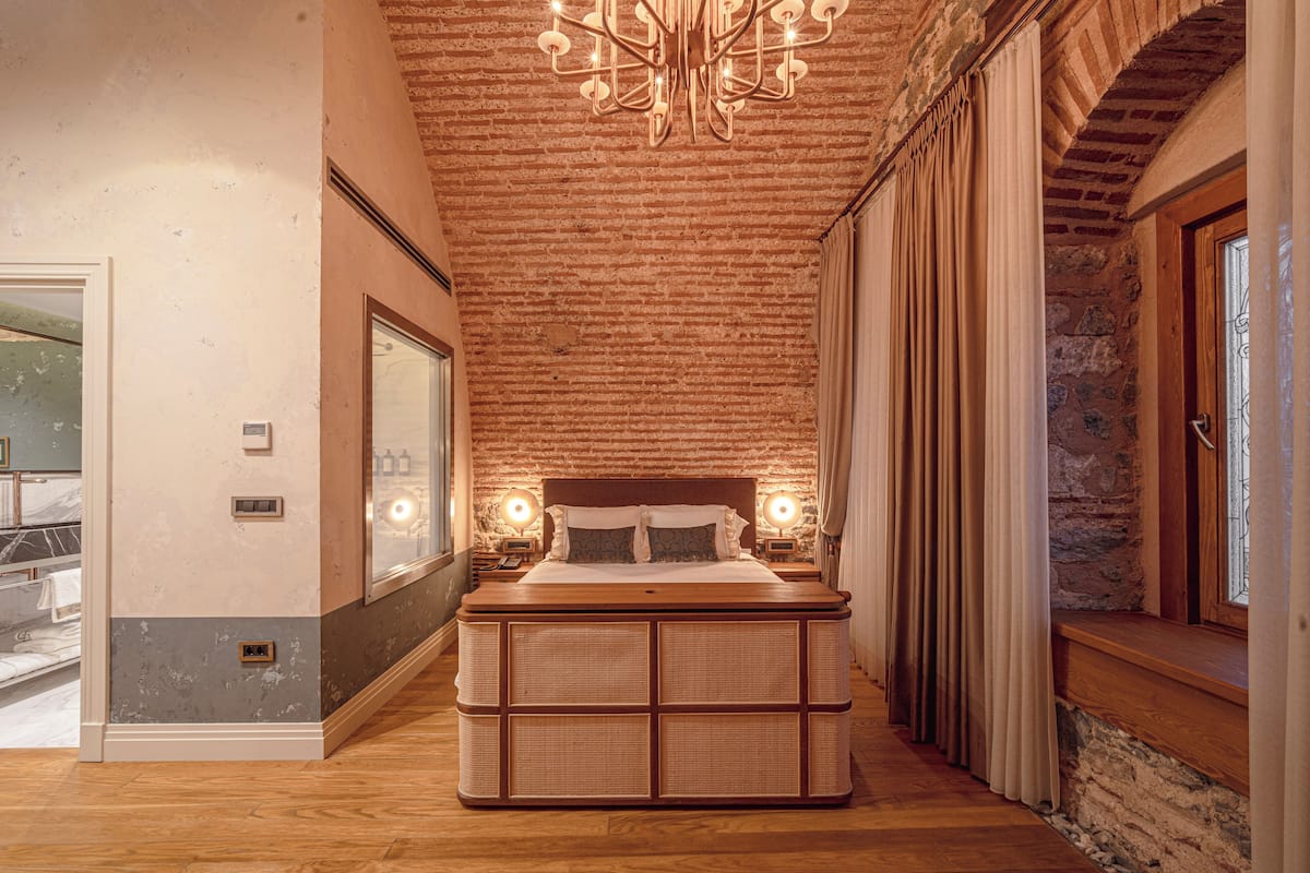 A bedroom with a large bed, wooden flooring, a brick ceiling, and a chandelier.