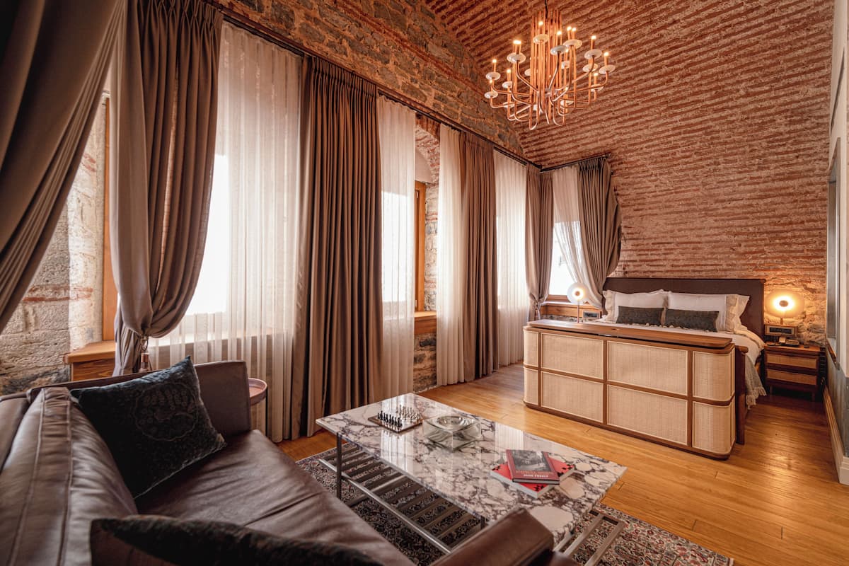 A modern hotel room with a brick wall, a large bed, a sofa, a coffee table, and a chandelier.