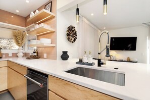 Una cocina moderna con lavavajillas integrado, armarios de madera, encimera de mármol y pileta de acero inoxidable.