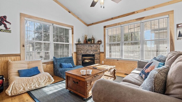 A cozy living room with a fireplace, large windows, and a ceiling fan. - BigFoot Inn, once you’ve seen it, you won’t want to leave! (PIGEON FORGE)