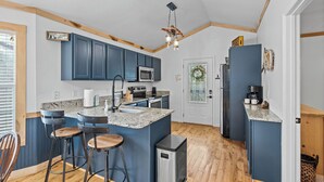 A modern kitchen with blue cabinets, a central island with stools, a stainless steel refrigerator, and a wooden ceiling. - BigFoot Inn, once you’ve seen it, you won’t want to leave! (PIGEON FORGE)
